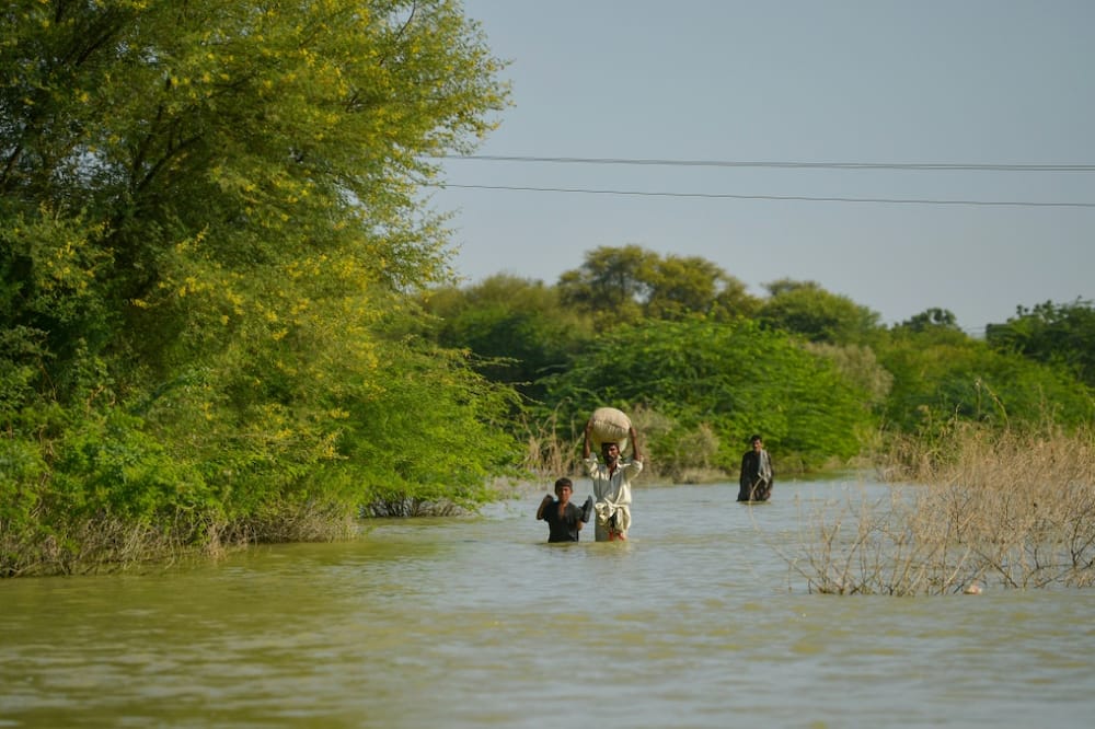 People wade through a flooded area pf Pakistan's Sindh province, on September 27, 2022