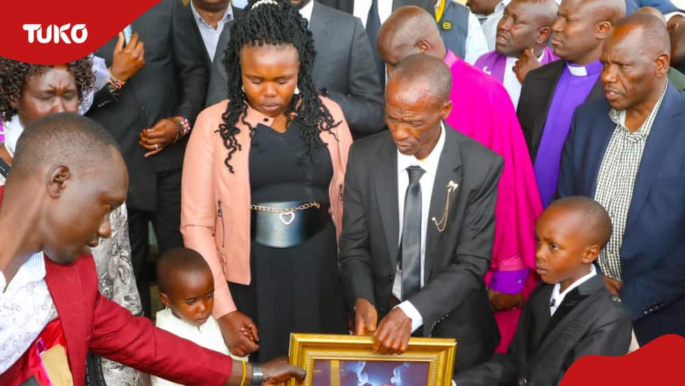 Kelvin Kiptum's father, Samson Cheruiyot, holds the portrait of his son as the athlete's wife and children watch.