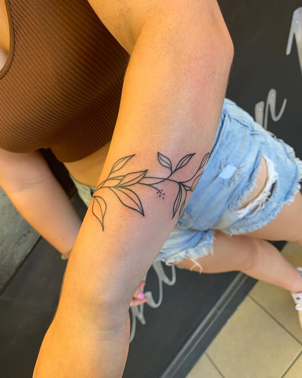 An simple tattoo of vines and leaves on a woman's forearm