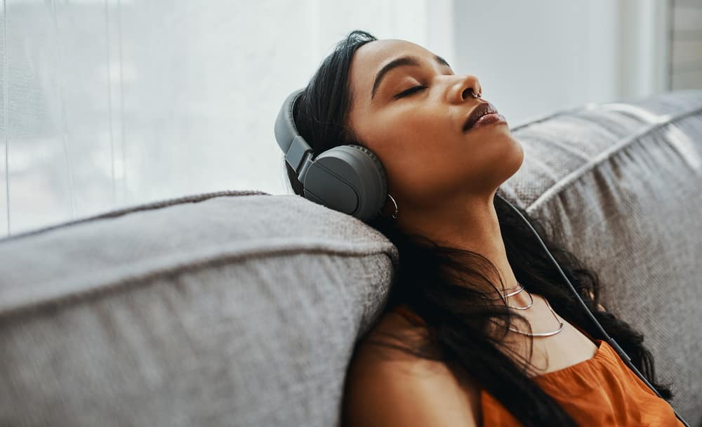 Shot of a young woman using headphones while relaxing on the sofa at home.