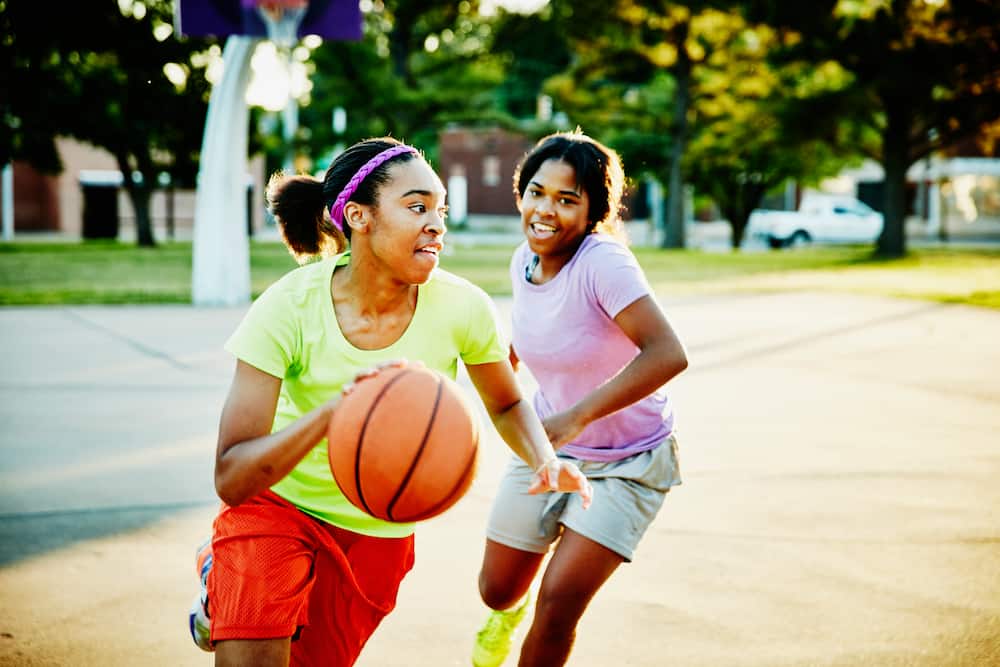 Female basketball player dribbling ball past defender on outdoor basketball court