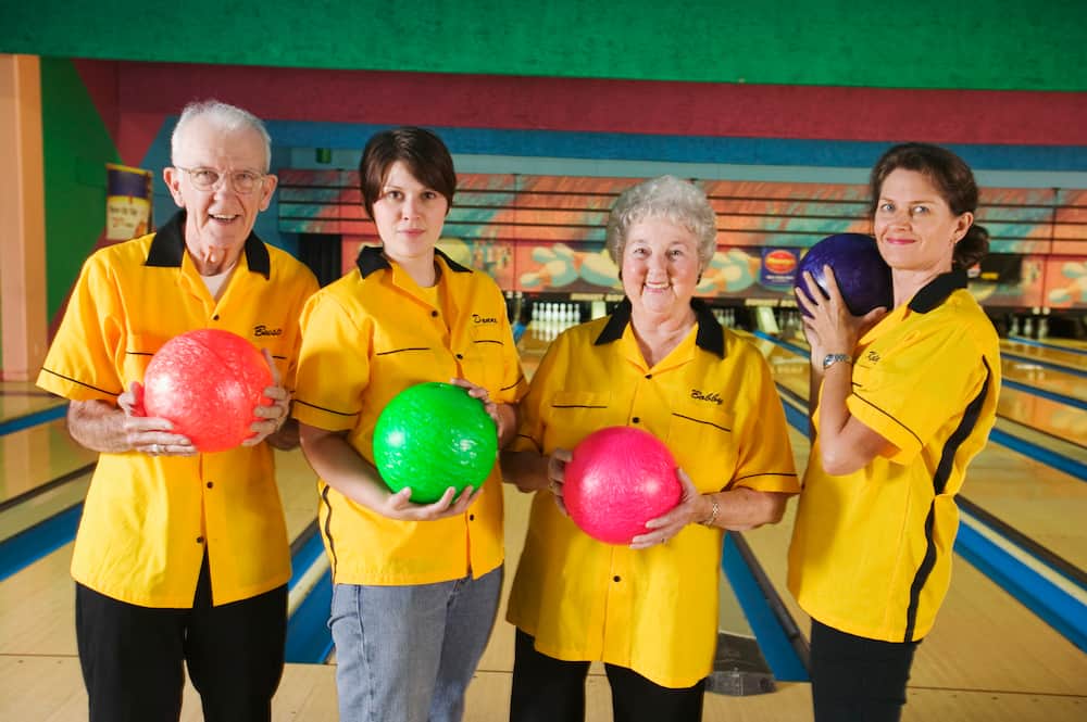 A bowling team in yellow uniform pose with assorted bowling balls.