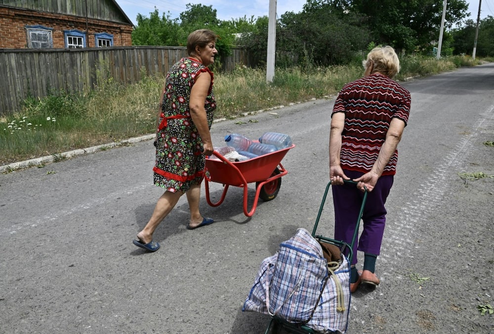 Women transport water bottles in a wheelbarrow and trolley