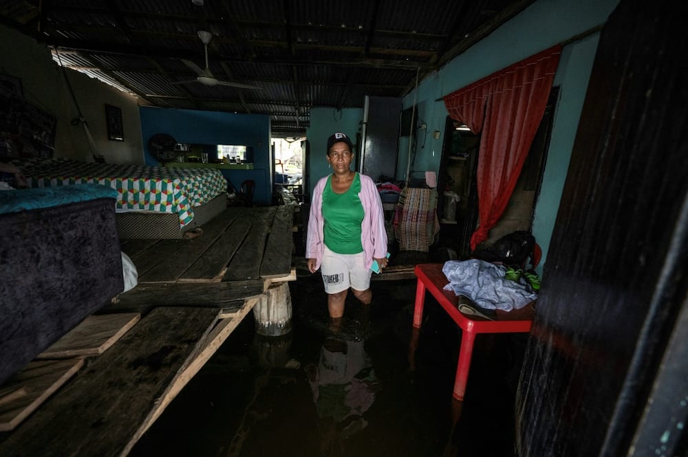 Rosiris Berrio moves around her flooded home, where beds and furniture has been placed on a system of raised planks
