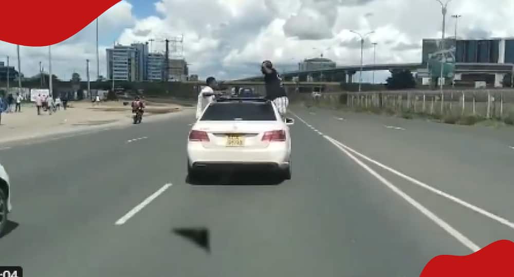Rowdy youths hang on speeding car.