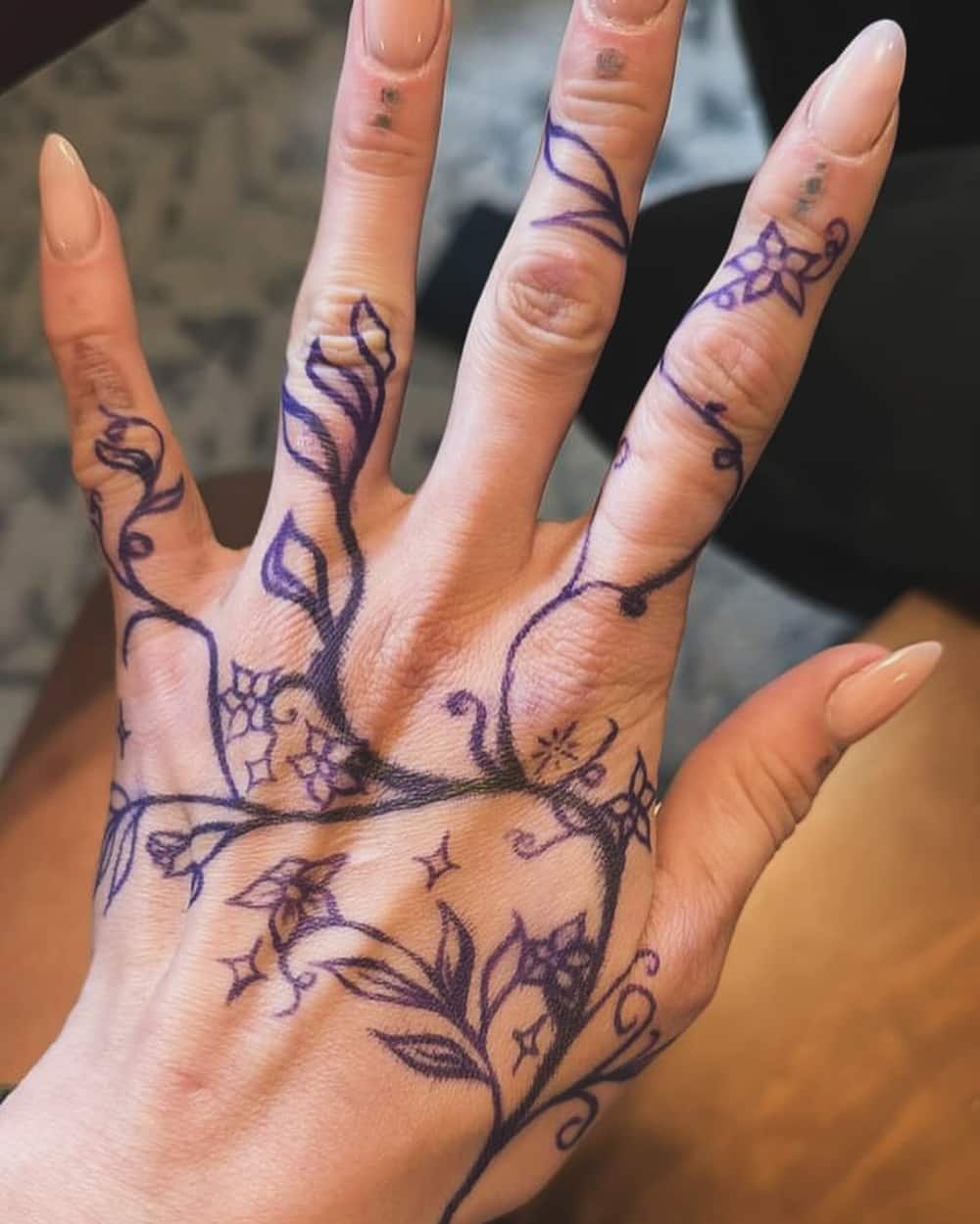 Hand of a woman adorned with purple vine tattoos.