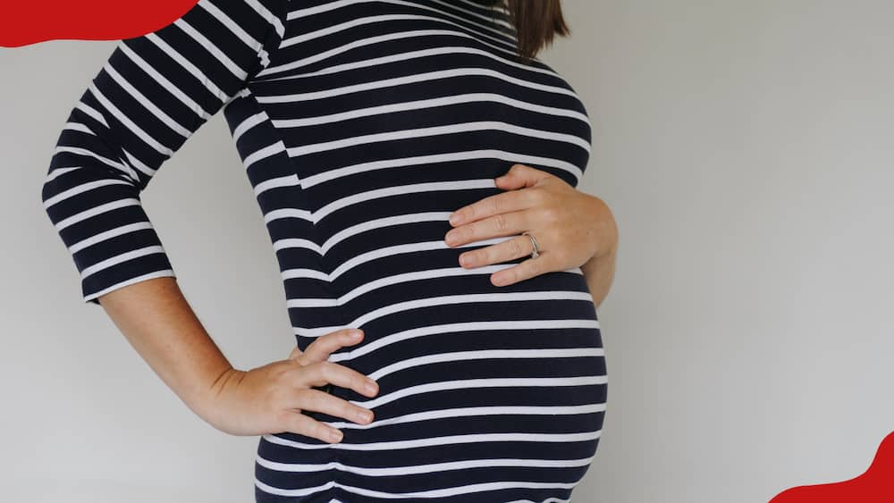 A woman in a stripped dress is holding her pregnancy bump