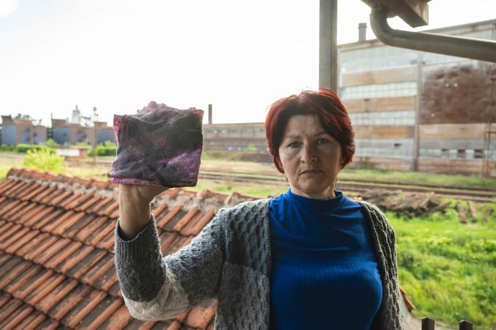 Dragana Milic holds up a cloth stained with dust after cleaning the window of her home near the steel plant
