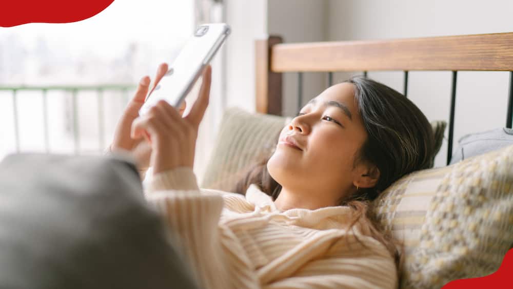 A woman is lying in bed while using a smartphone
