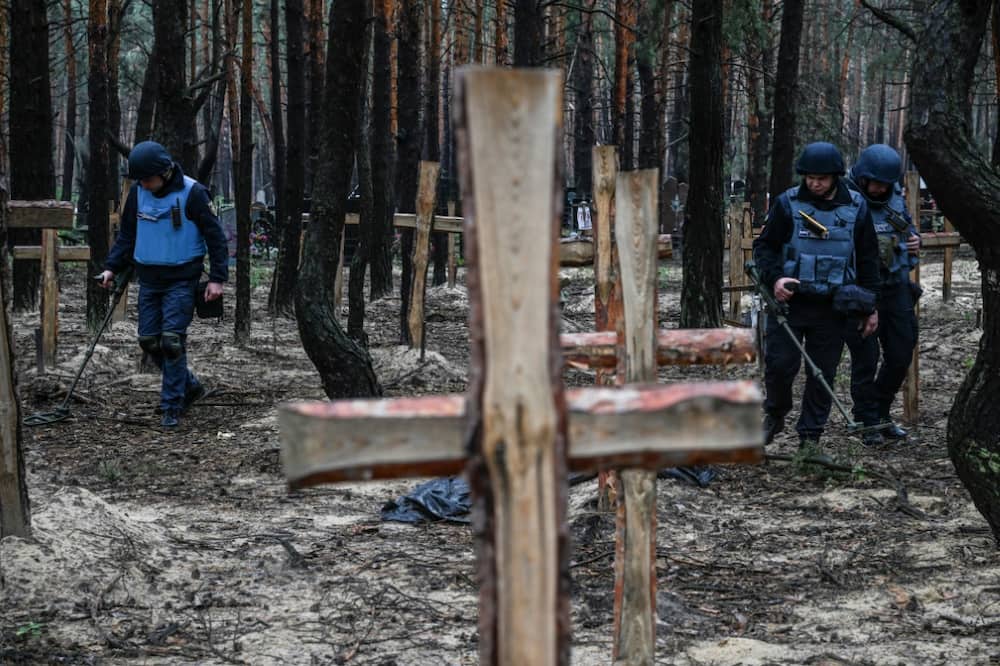 Ukrainian servicemen search for land mines at a burial site in a forest on the outskirts of Izyum