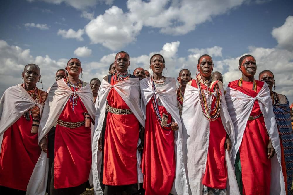 Maasai women wearing traditional clothes and red ochre pigment on their faces sing and dance during the Eunoto ceremony.