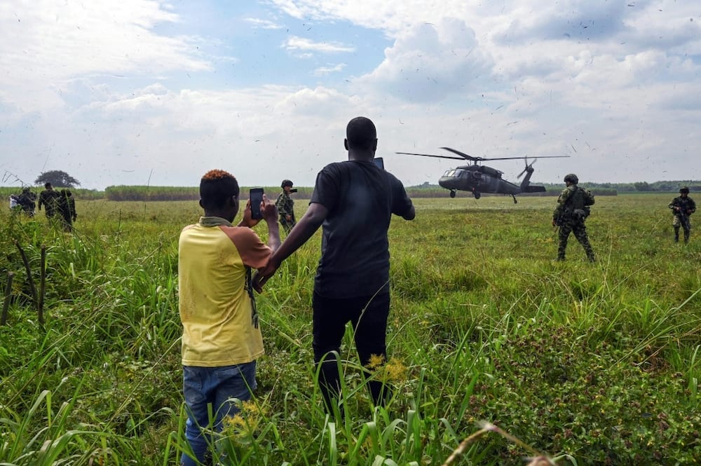 A man and a teenager record with their mobile phones the landing of a Colombian Army helicopter as soldiers stand guard in Tetillo near Corinto, department of Cauca, Colombia