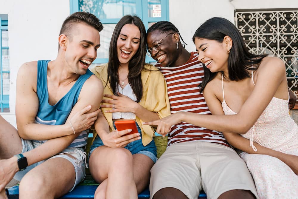 A group of multiracial people having fun watching social media video content on a smartphone.