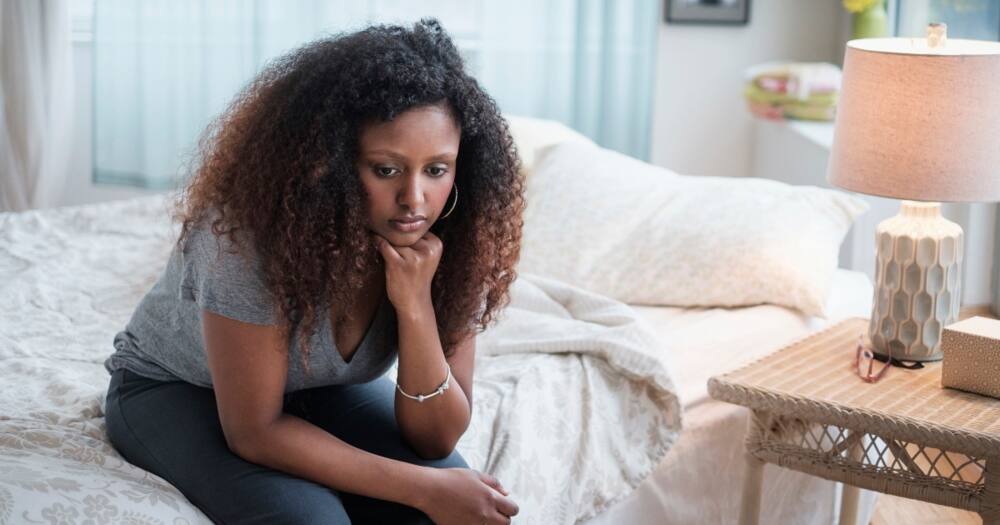 Sad black woman sitting on bed. Photo: Getty Images.