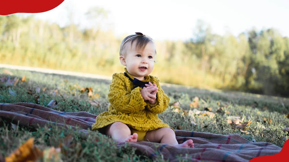 A baby is wearing a yellow crochet and sitting on textile