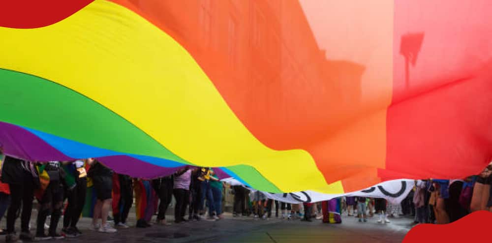 People stand holding rainbow flag.