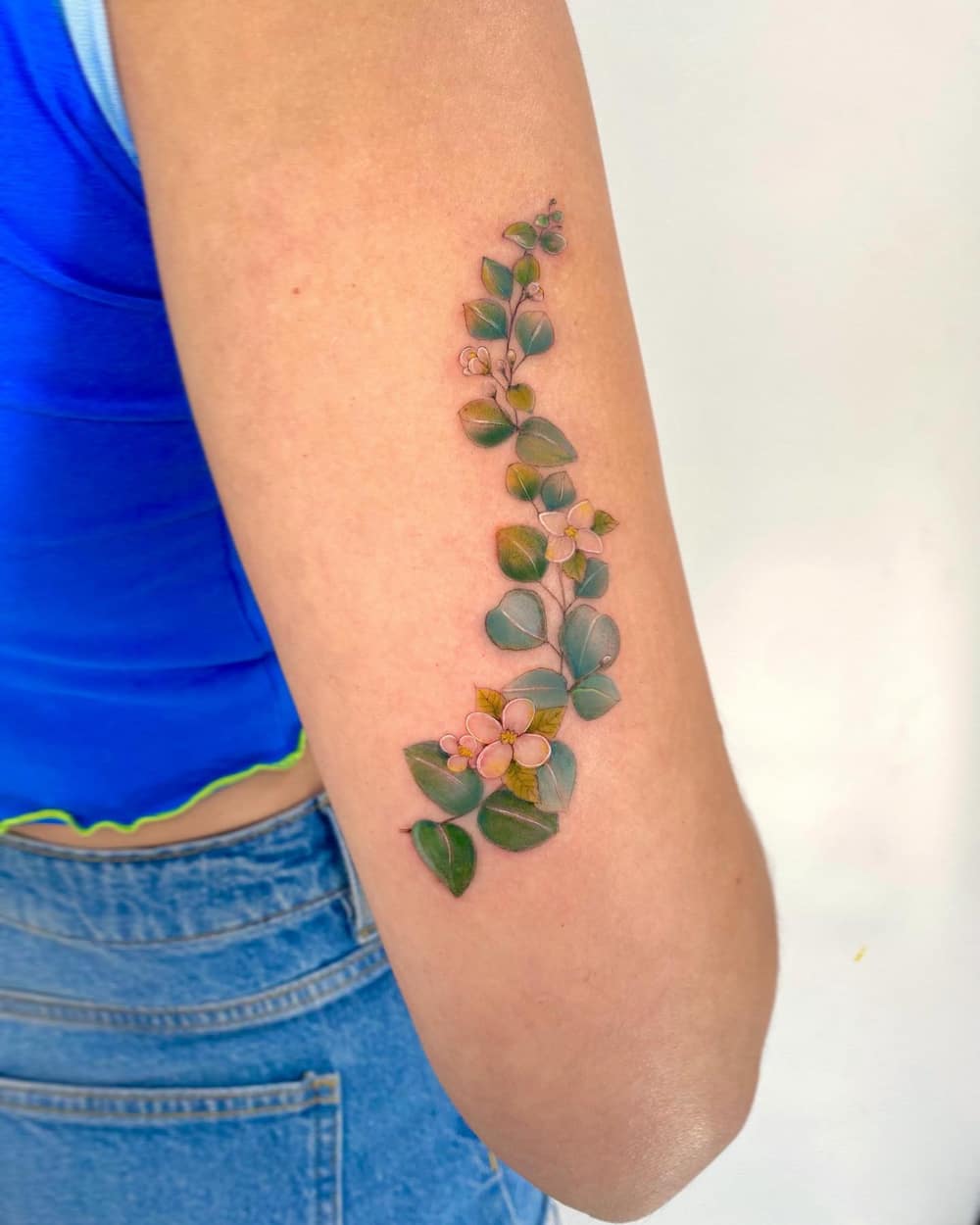Tattoo of Eucalyptus leaves and Jasmine flowers on a woman's arm.