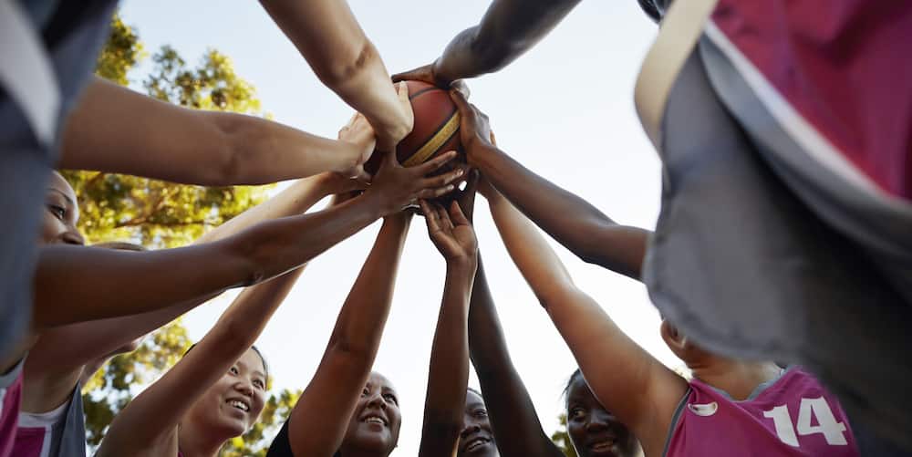 A basketball team is standing in a circle with their hands on the ball