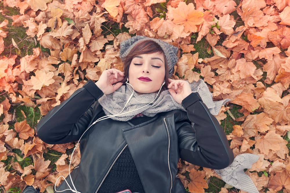 Young woman listening to music with closed eyes lying in an autumn park.